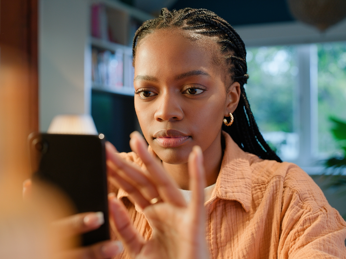 Person focused on using a smartphone in a warmly lit indoor setting with bookshelf and plants.