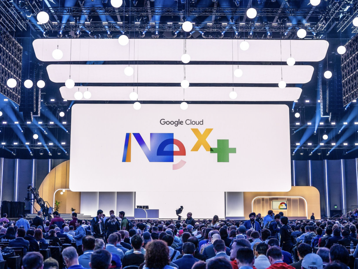 Crowd seated in a large arena facing a stage with the Google Cloud Next+ logo on screen.