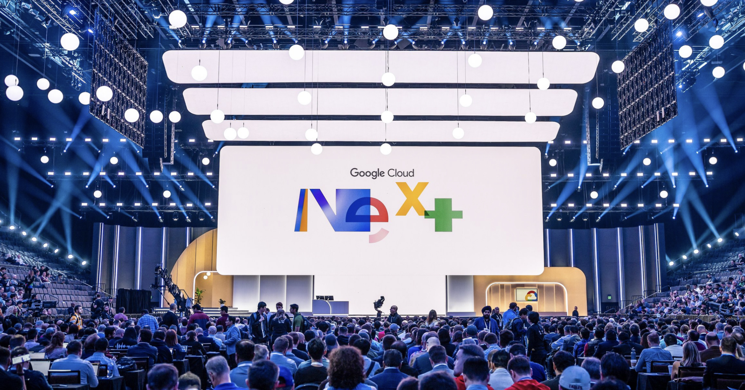 Crowd seated in a large arena facing a stage with the Google Cloud Next+ logo on screen.