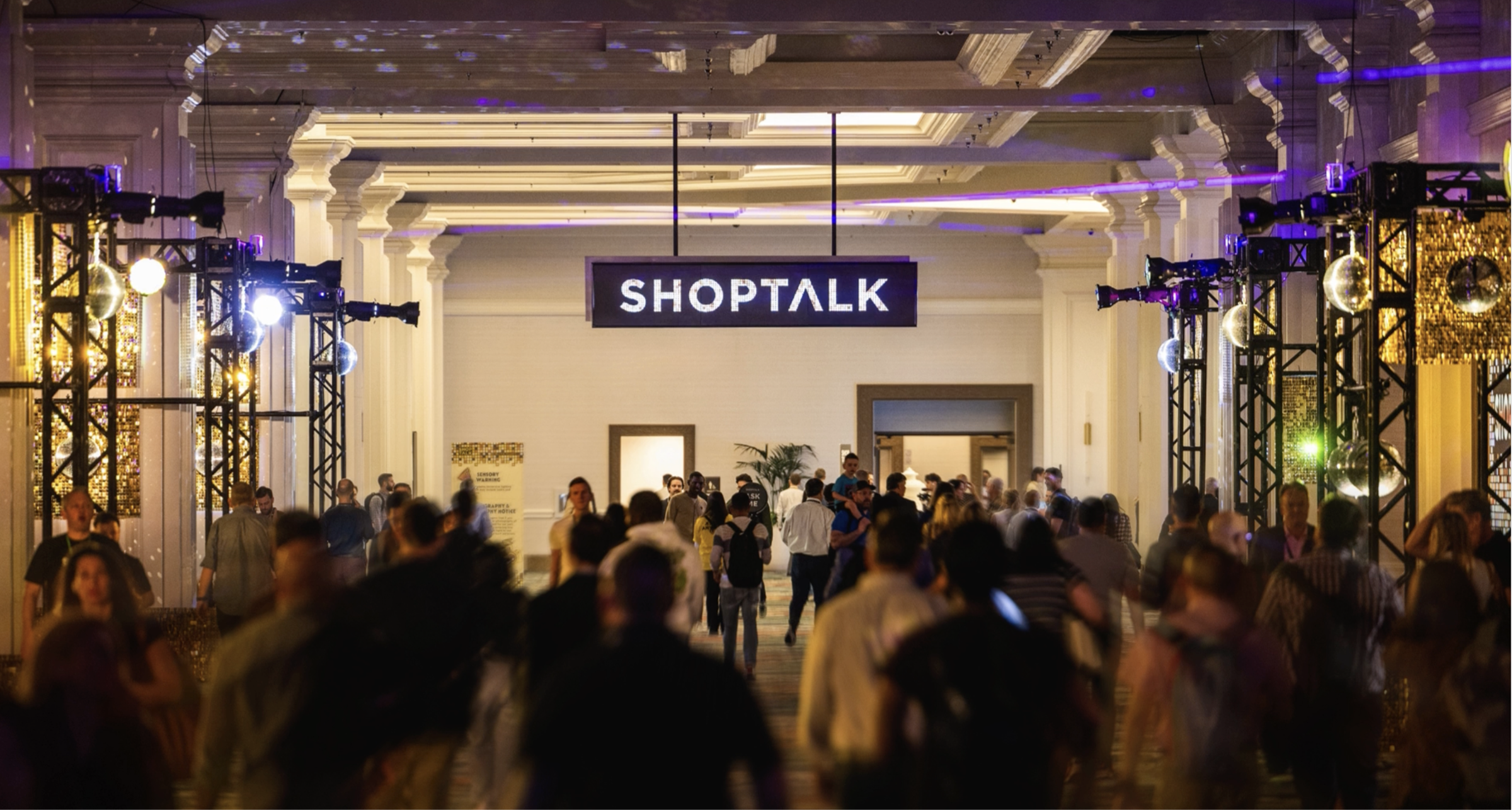 Crowd of attendees entering the Shoptalk conference hall under an illuminated Shoptalk sign.
